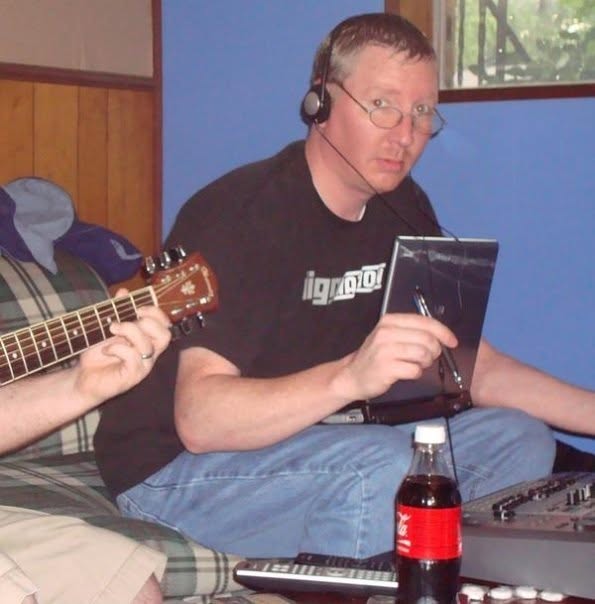 A person wearing a headset beside a guitar and audio equipment.